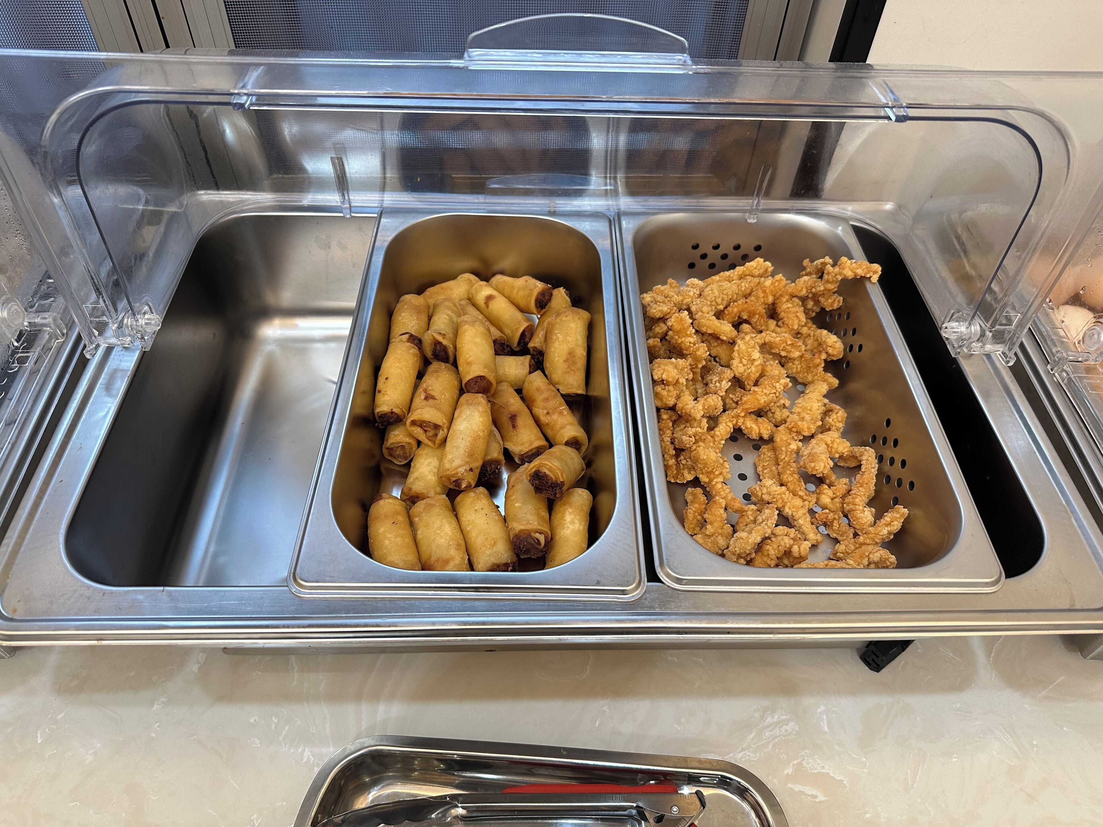 Ein Buffet mit zwei Platten gebratenem Essen, eine mit Frühlingsrollen und die andere mit gebratenem Hähnchen.