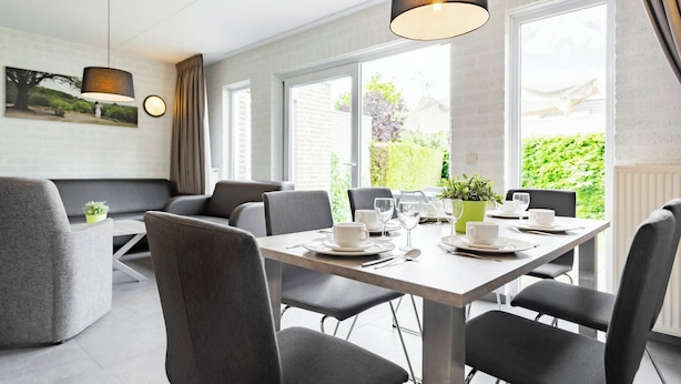 A modern dining area with a rectangular table set for four, surrounded by grey upholstered chairs. - Summio Bungalowpark De Riethorst (Plasmolen)