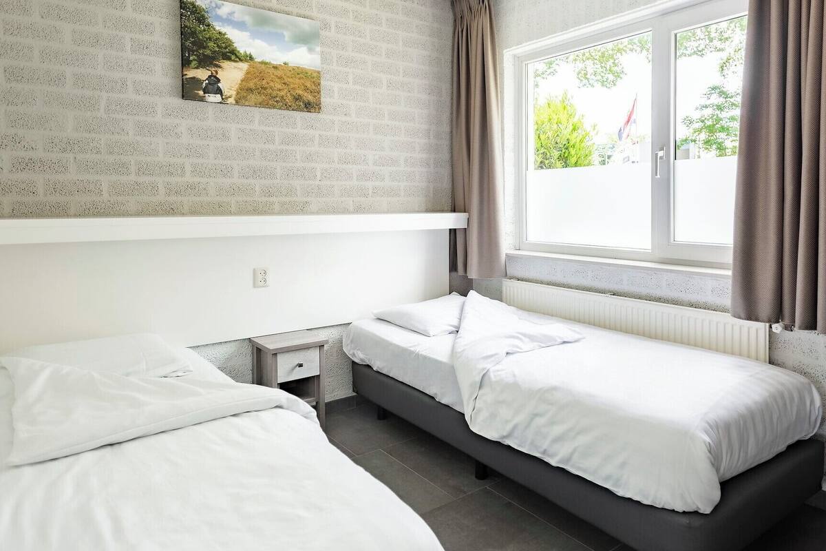 A bedroom with two single beds, a small bedside table, a window with curtains, and a picture on the wall.
