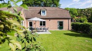A brick house with a tiled roof, a covered patio with a table and chairs, and a well-maintained lawn. - Summio Bungalowpark De Riethorst (Plasmolen)