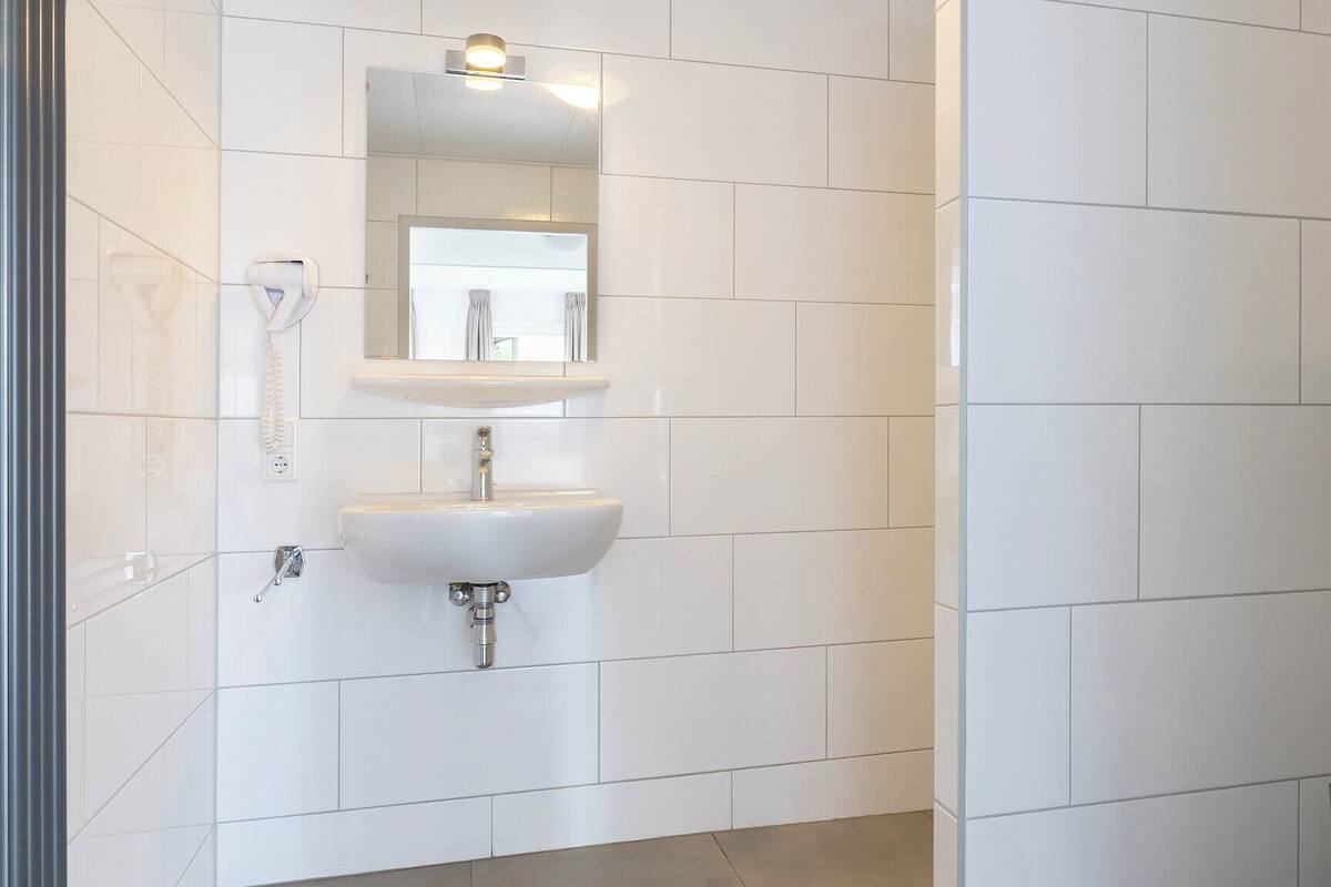 A bathroom with white tiles, a sink, a mirror, and a shower area.