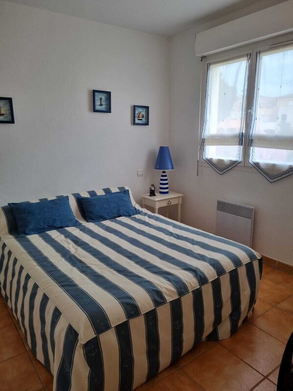 A bedroom with a bed, a nightstand, a lamp, and a window. - Very nice apartment for 4 people, 2 bedrooms, beautiful living room and terrace. (Cavalaire-sur-Mer)