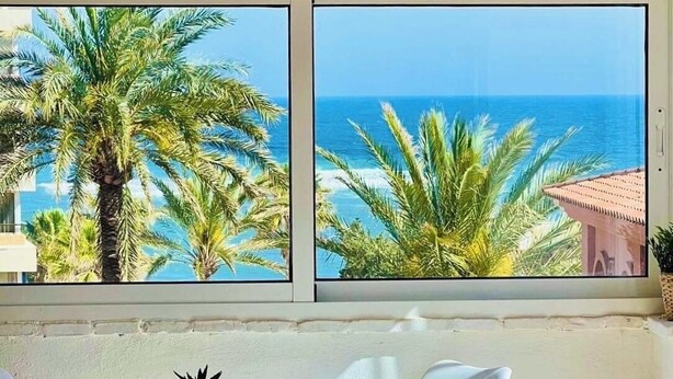 Un comedor con una mesa y sillas, un cactus en maceta, y vista al océano a través de amplias ventanas.
