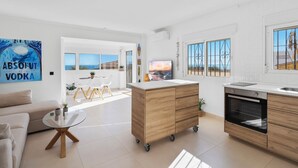 Una cocina moderna con horno empotrado, una zona de comedor con mesa de vidrio y vistas al mar a través de grandes ventanales.