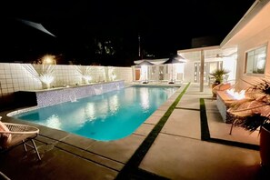 A swimming pool with a tiled deck, lounge chairs, and a fire feature.