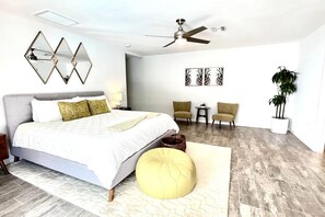 Ein modernes Schlafzimmer mit Bett, Deckenventilator, kleinem Tisch, zwei Stühlen und einer Topfpflanze.