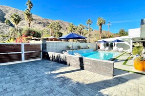 A swimming pool with a tiled deck, surrounded by palm trees and a mountain backdrop.