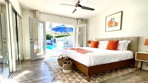 Quarto com cama, ventoinha no teto, quadro emoldurado e vista para uma piscina através das portas de vidro.