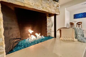 A modern fireplace with a stone facade, a glass water feature, and a cozy seating area with a blanket and chairs. - Fantastic MidCentury Modern, Pool, Views, Privacy! (Palm Springs)