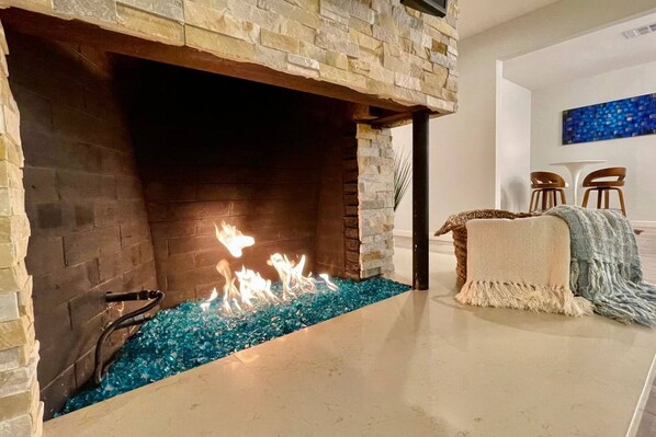 A modern fireplace with a stone facade, a glass water feature, and a cozy seating area with a blanket and chairs.