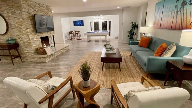 Uma sala de estar moderna com parede de destaque em pedra, mesa de bilhar e sofá verde-água.