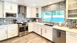 Cozinha moderna com armários brancos, fogão de aço inoxidável, micro-ondas e uma grande janela com vista para o exterior.