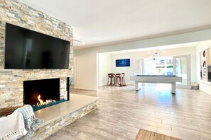 A modern living room with a stone fireplace, a flat-screen TV, and a pool table.