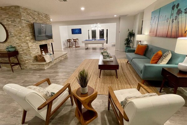 A modern living room with a stone accent wall, a pool table, and a teal sofa.