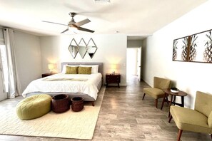 A modern bedroom with a bed, two nightstands, a chair, a small table, and a ceiling fan.