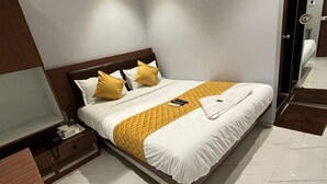 A modern hotel room with a large bed, a bedside table, a nightstand, and a built-in TV. - Powai Inn (Mumbai)