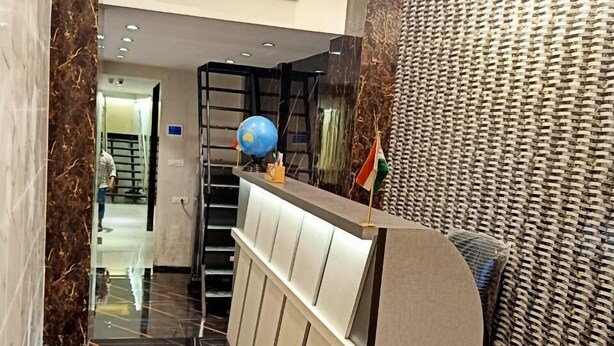 A modern hotel lobby with a marble floor, a staircase, a reception desk, and a flat-screen TV mounted on the wall. - Powai Inn (Mumbai)