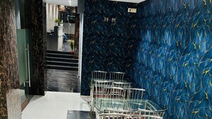 A modern interior with a dark blue wall featuring a leaf pattern, white marble flooring, and metal-framed chairs with leather seats. - Powai Inn (Mumbai)
