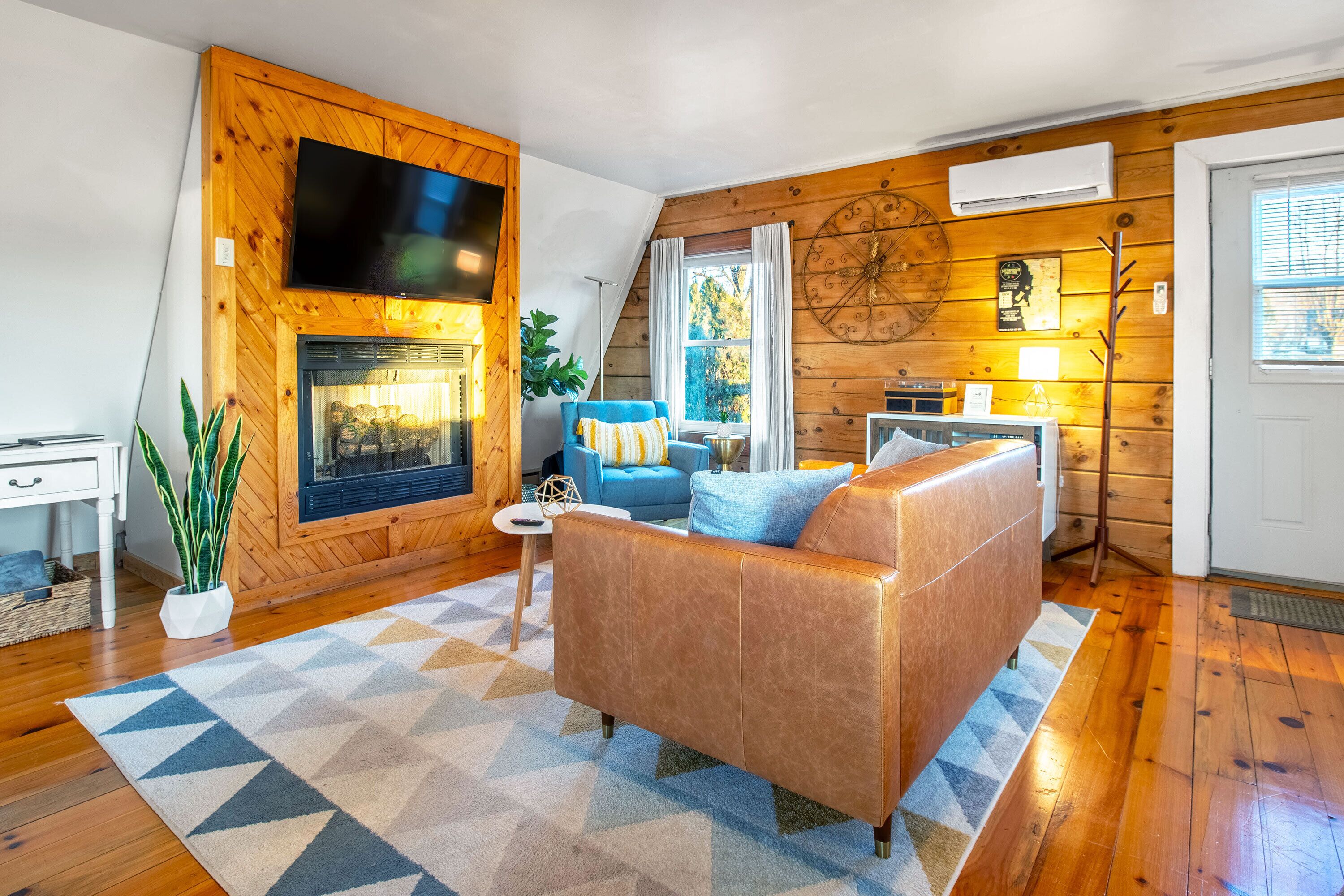 A cozy living room with a fireplace, a blue sofa, and a wooden wall.