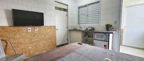 A hotel room with a bed, a television, a kitchenette, and a sliding door.
