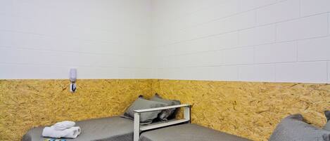 A small, single-room hotel room with two beds, a wooden wall, a white ceiling, and a wall-mounted light fixture.