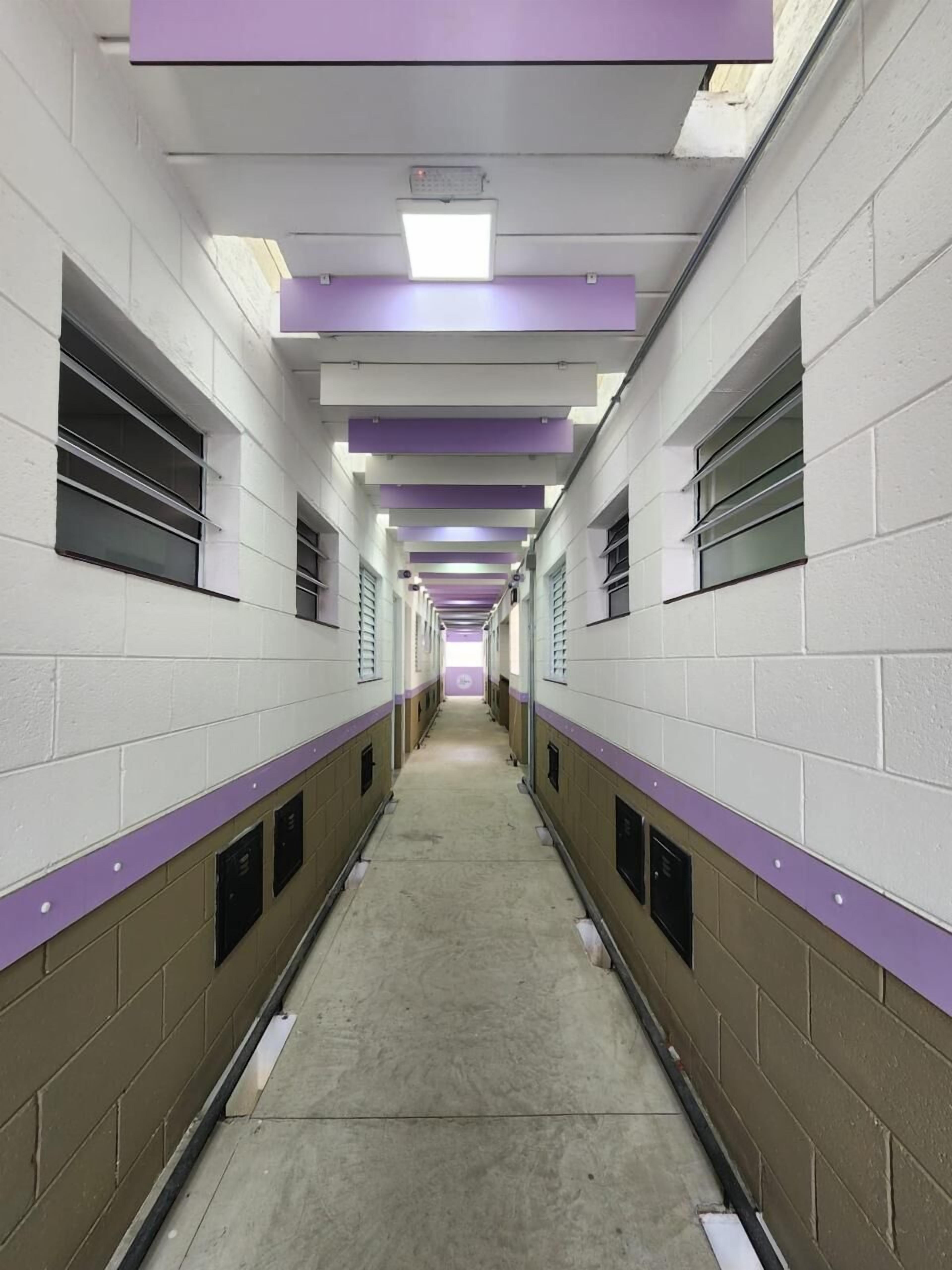 Un long couloir étroit aux murs blancs et aux touches de couleur violette, où l’on trouve de part et d’autre une rangée de casiers.