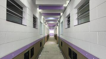 Un long couloir étroit aux murs blancs et aux touches de couleur violette, où l’on trouve de part et d’autre une rangée de casiers.