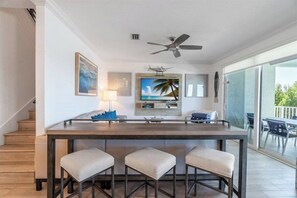 A modern kitchen with a bar area, a ceiling fan, and a large window overlooking a balcony. - Starfish Isle 5 bedroom 5 bath pool, elevator, 50 ft of dockage paddleboards, kayaks, bikes and walking distance to the beach (Marathon)