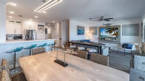 A modern kitchen with white cabinets, a dining area with a wooden table, and a TV mounted on the wall.