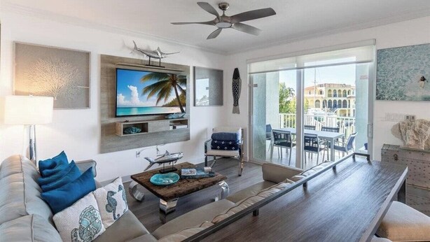 A modern living room with a flat-screen TV, a ceiling fan, and a balcony with outdoor seating.