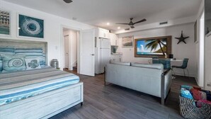 A bedroom with a bed, a small kitchenette, a dining area with a table and chairs, and a ceiling fan.