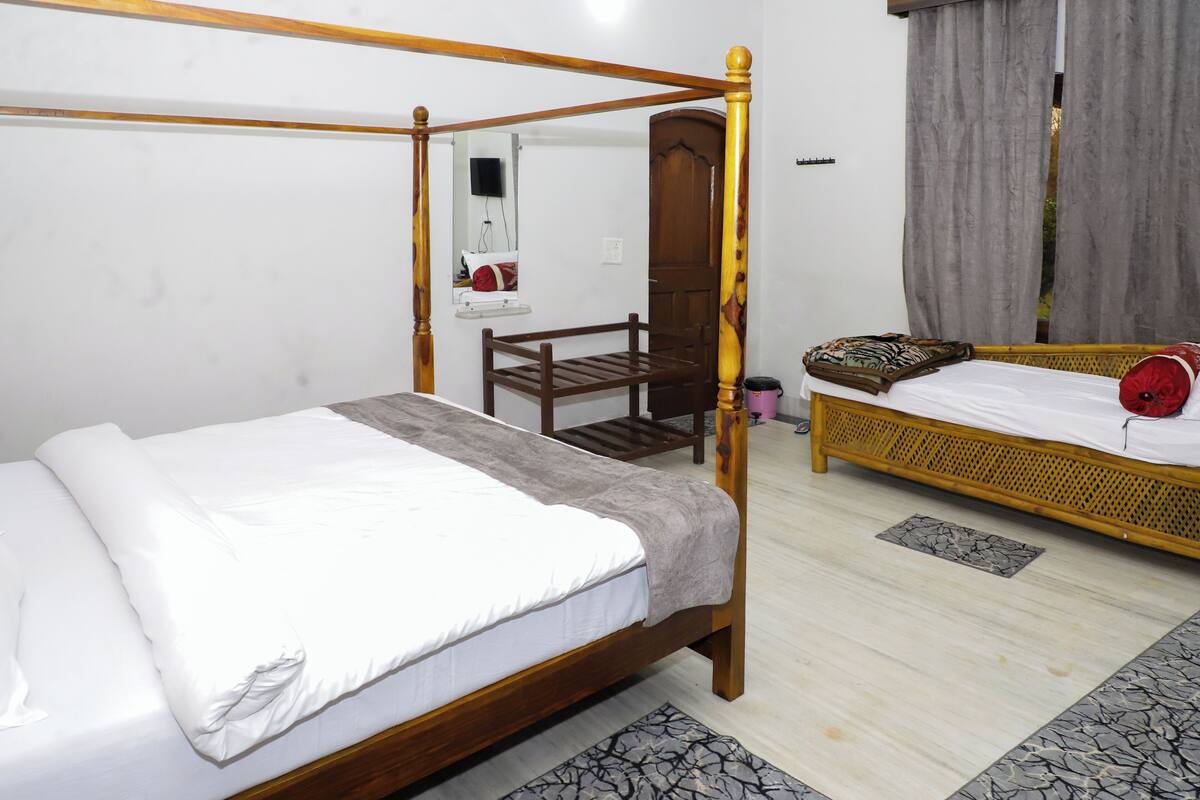 A room with a four-poster bed, a smaller bed with a patterned bedspread, a wooden chair, and a small table.