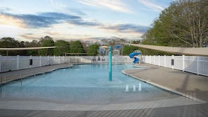 Une piscine avec un toboggan, entourée de clôtures blanches et d’arbres.