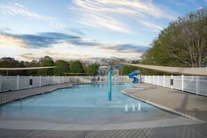 Una piscina con tobogán acuático, rodeada de vallas blancas y árboles.