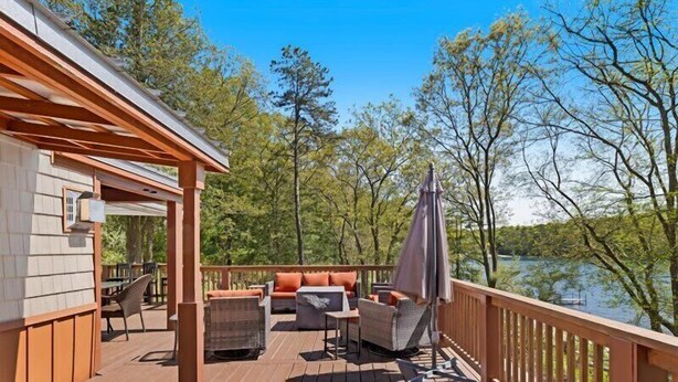 Une terrasse en bois avec des sièges d’extérieur, une rambarde et une vue sur un lac.