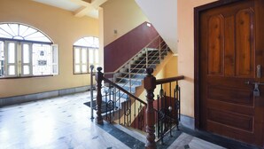 A spacious interior with a marble floor, a staircase with a wooden handrail, and a large wooden door.