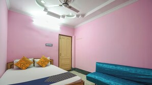 A bedroom with pink walls, a wooden bed, two pillows, a blue bedspread, a ceiling fan, and a blue sofa.