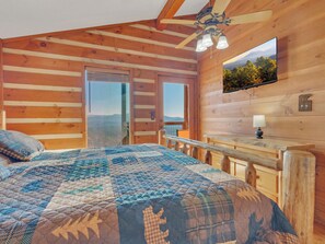 A wooden cabin bedroom with a bed, a desk, and a TV mounted on the wall.