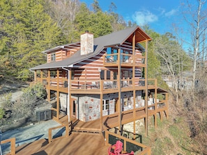 A multi-story log cabin with a stone foundation, multiple balconies, and a wooden deck. - Breathtaking Views | Close To Dollywood | Hot Tub | Pool Table | WiFi (Sevierville)