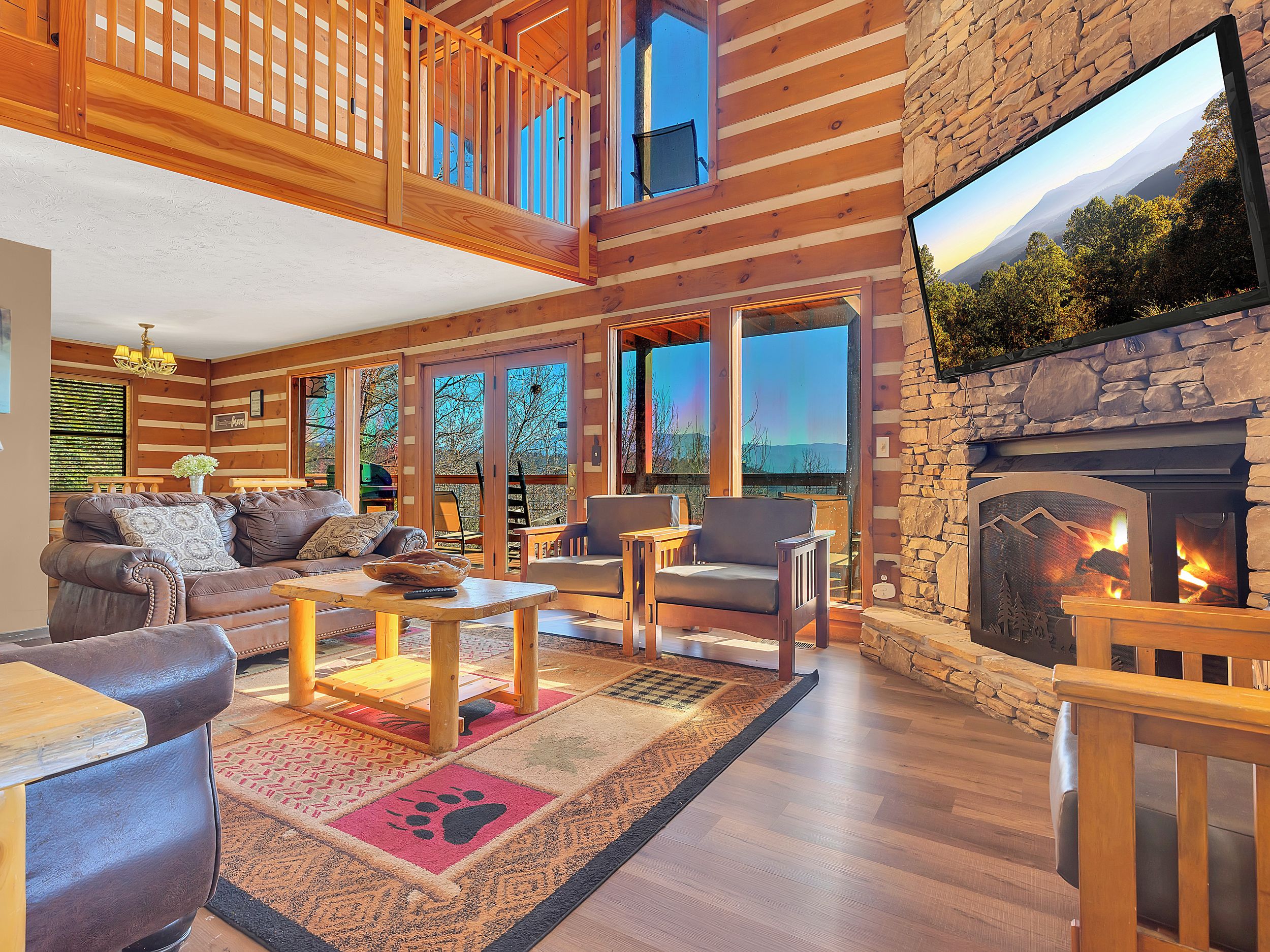 A spacious living room with a fireplace, wooden furniture, and large windows offering a view of the outdoors.