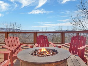 A deck with a fire pit, red Adirondack chairs, and a view of mountains.