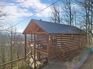 A wooden cabin with a metal roof, a balcony, and a stone foundation. - Stunning Mountain Views | Pool Table | Hot Tub | WiFi | Game Room (Sevierville)
