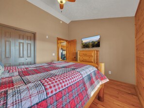 Une chambre à coucher comprenant un lit, une armoire en bois, un téléviseur et une porte donnant sur la cuisine.