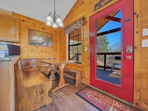 A cabin interior with a wooden dining table, benches, a red door, and a welcome mat. - Stunning Mountain Views | Pool Table | Hot Tub | WiFi | Game Room (Sevierville)