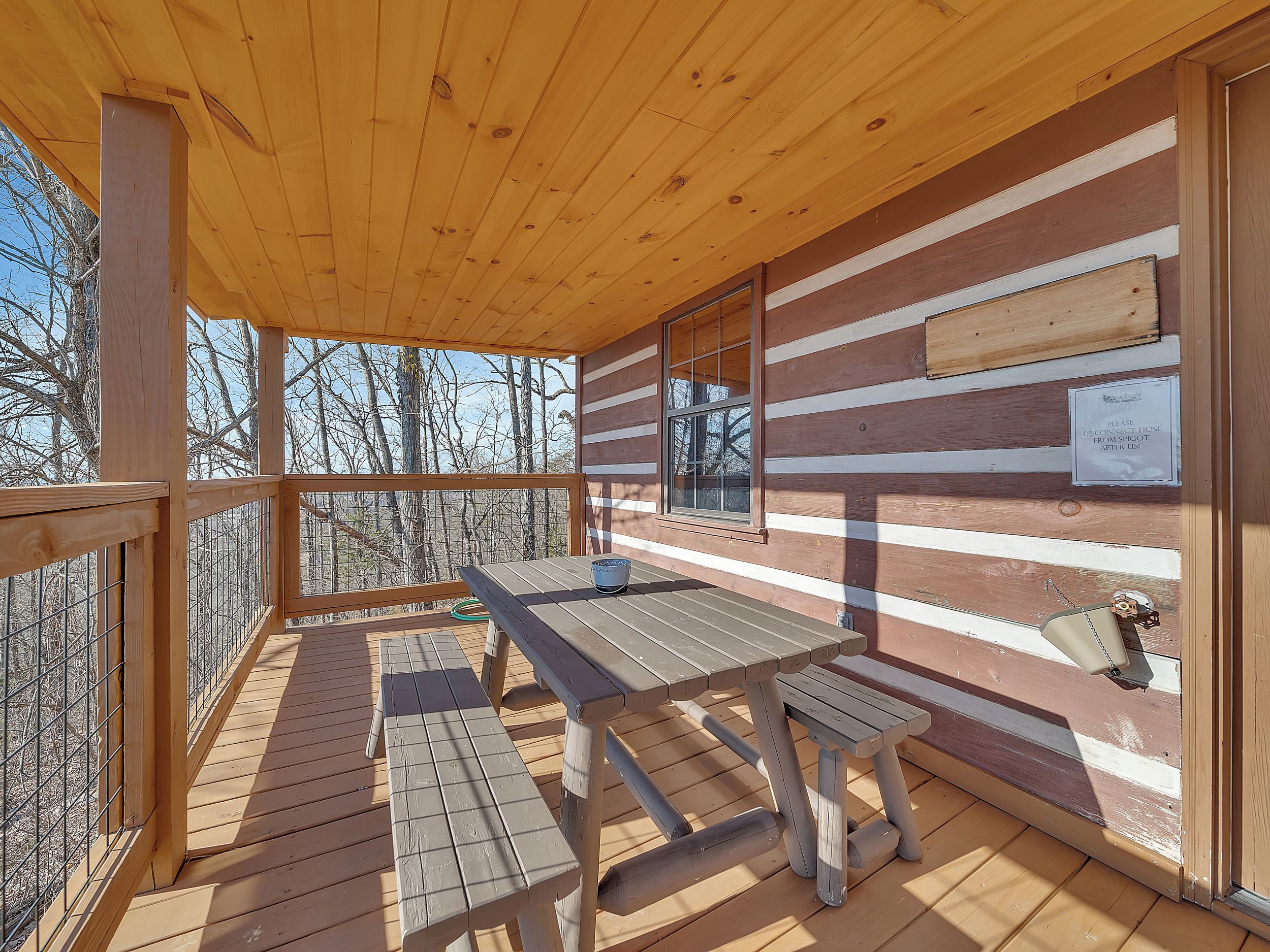 Eine Holzdielen-Terrasse mit Tisch und Bänken, mit Blick auf einen bewaldeten Bereich.