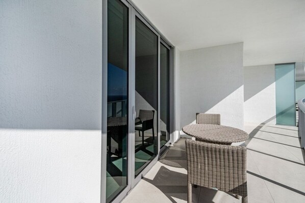 Un balcon avec une table et des chaises en osier, une porte-fenêtre coulissante et une vue sur l’intérieur.