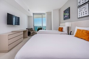 Ein Hotelzimmer mit zwei Betten, einem Fernseher, einem Schreibtisch und Blick auf den Himmel.