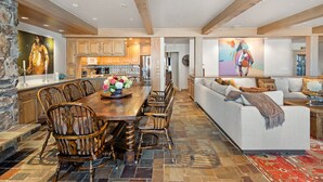 A spacious living area with a large dining table, wooden chairs, a sofa, and a kitchen in the background.