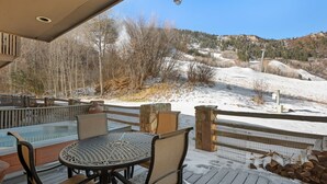 A covered outdoor area with a hot tub, seating, and a view of a snowy landscape and ski lift.