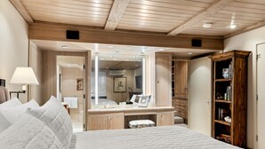 A bedroom with a large bed, a vanity with a mirror, wooden cabinets, and a bookshelf.